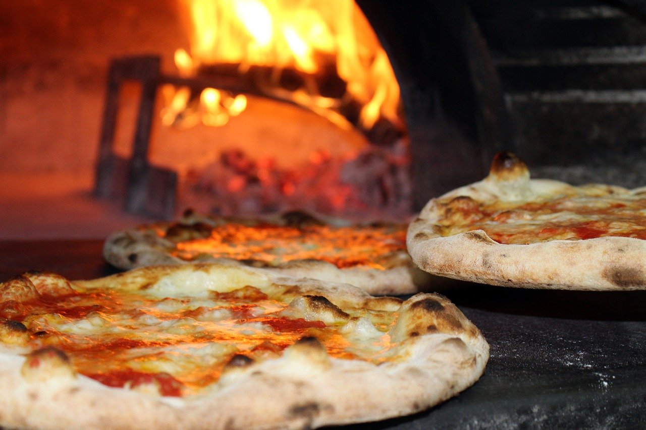 Pizzen vor einem Pizzaofen mit Feuer