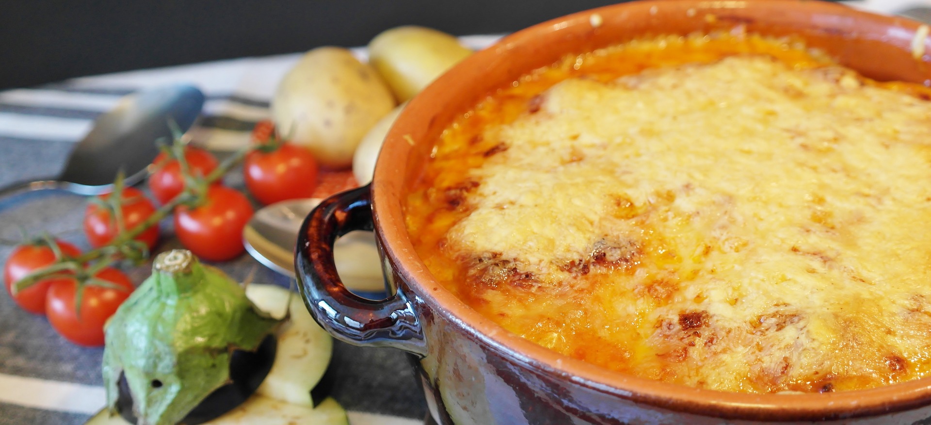 Gratin mit Käse überbacken und daneben Garnitur mit frischen Tomaten und Kartoffeln und Aubergine