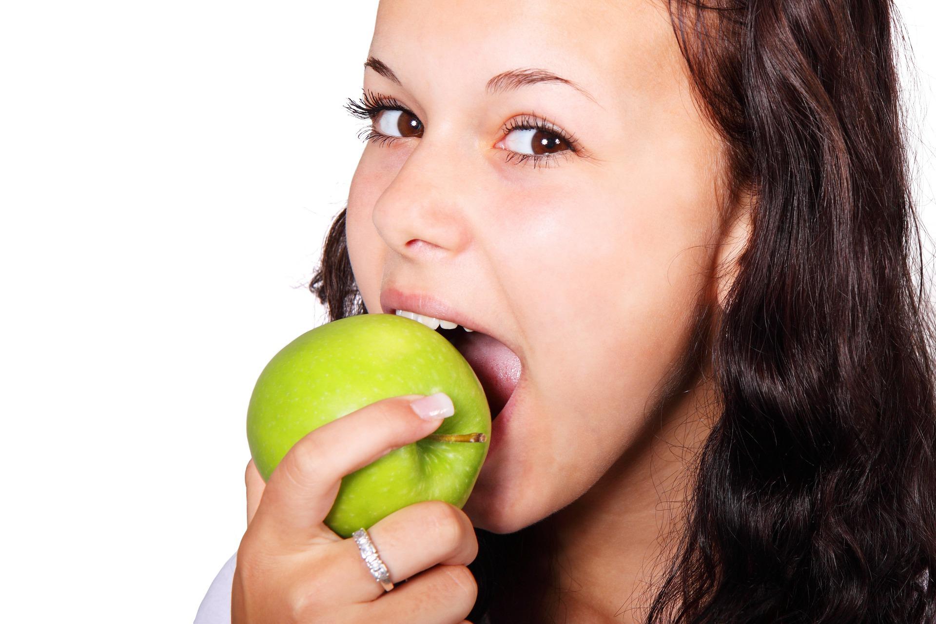 Junge Frau mit dunklen Haaren beißt in einen grünen Apfel